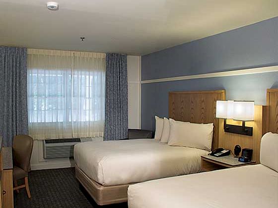 A hotel room with two double beds, nightstands, a window with curtains, a desk and chair, and soft lighting&mdash;cozy, modern decor.