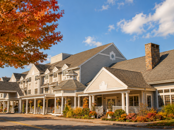 An apartment complex sits beneath bright autumn trees, with colorful leaves and a blue sky above the buildings.